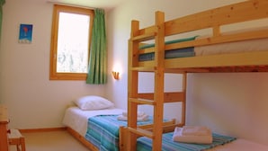 Una habitación con literas, una ventana con cortinas, una mesita y una lámpara fijada a la pared.