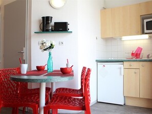 Uma cozinha compacta com cafeteira, micro-ondas e máquina de lavar louça. Há uma mesa de jantar com cadeiras vermelhas e um vaso com flores.
