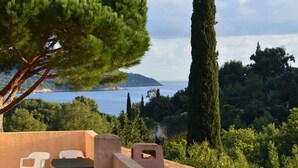 A terrace with a table and chairs, overlooking a coastal landscape with trees and a view of the sea. - Apartment with Pool and Terrace 300m from the Beach (La Croix-Valmer)