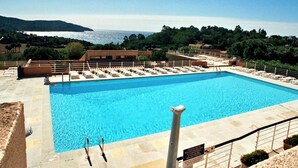 A large rectangular pool with clear blue water, surrounded by a stone deck and a metal railing. There are lounge chairs and a small building in the background. - Apartment with Pool and Terrace 300m from the Beach (La Croix-Valmer)