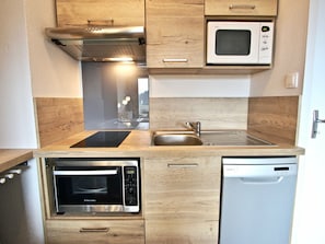 A compact kitchen with a built-in microwave, oven, and dishwasher, featuring wooden cabinetry and a stainless steel sink.