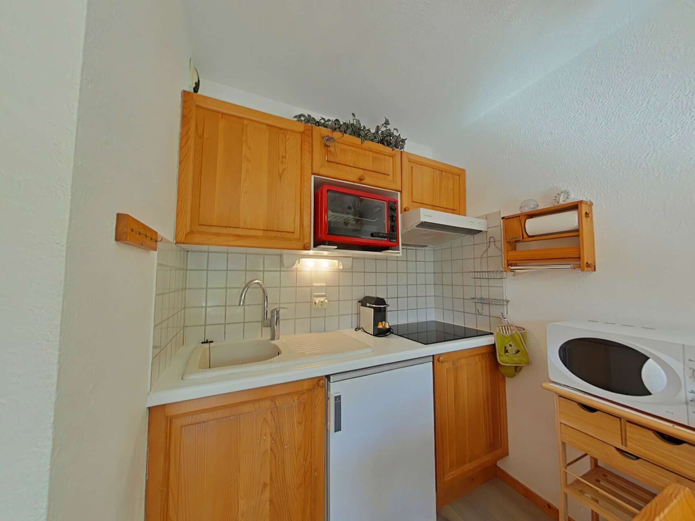Une cuisine compacte avec des meubles en bois, un four à micro-ondes, un évier et un petit réfrigérateur.
