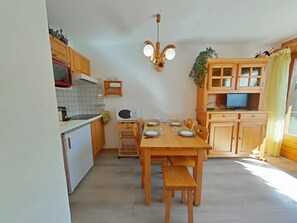 Uma cozinha compacta com armários de madeira, micro-ondas, mesa de jantar com cadeiras e um pequeno banco.