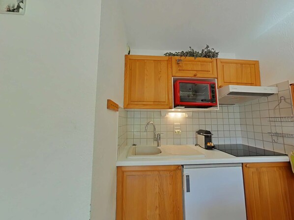A compact kitchen with wooden cabinets, a white countertop, a sink, a microwave, and a refrigerator. - Cozy apt for 5, 300m to slopes, parking, pets allowed (Le Grand-Bornand)
