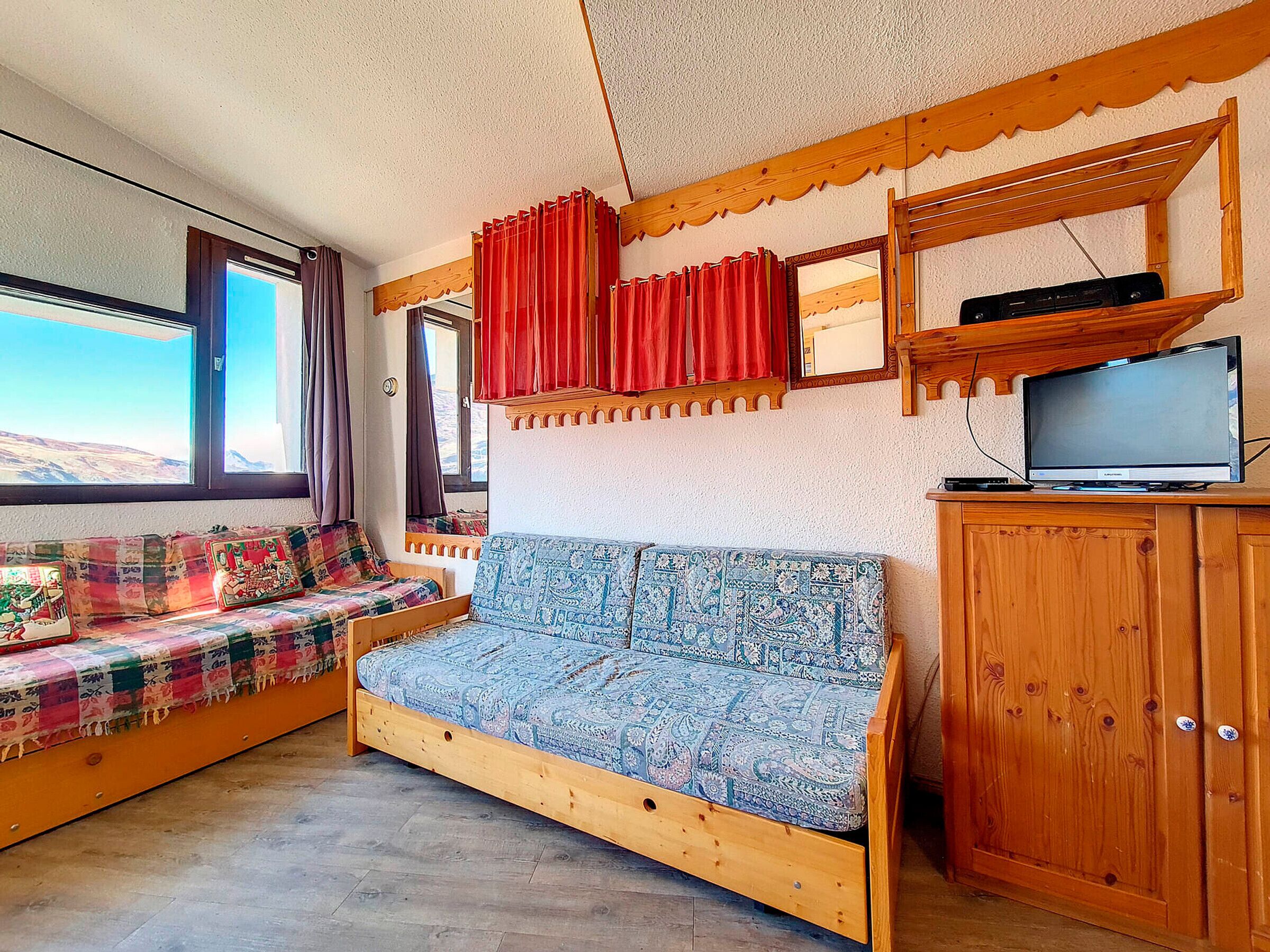 A cozy room with a wooden sofa, a television on a wooden stand, and a window with curtains.
