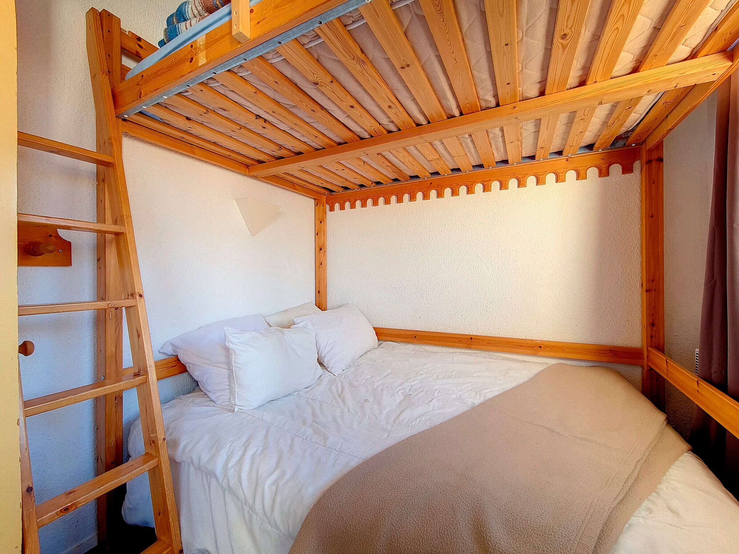 Una cama litera de madera con escalera, ropa de cama blanca y cabecera con diseño decorativo.