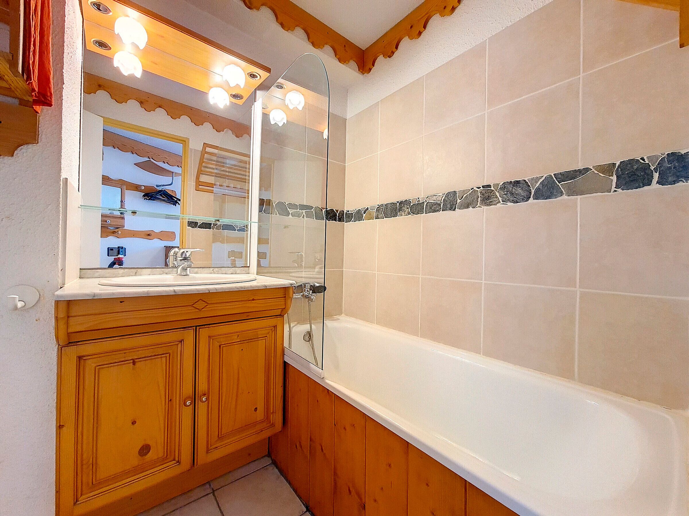 A bathroom with a wooden vanity, a large mirror, a bathtub, and a stone mosaic border.