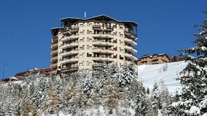 Et hotel med flere etager og balkoner, omgivet af sneklædte træer og en klar blå himmel.