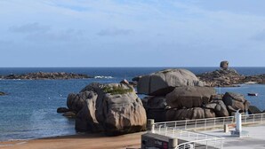 A coastal landscape with large boulders, a sandy beach, and a calm sea.