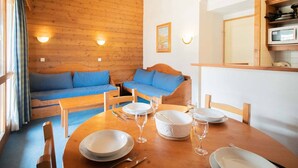 Indbydende kabineinteriør med trævægge, en sofa, et spisebord dækket med tallerkener og glas, og en mikrobølgeovn i køkkenet.