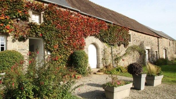 A stone building with a sloped roof, covered in ivy and red flowers, and surrounded by gravel paths and potted plants. - Charming studio at the Manor with private garden and WiFi (Baubigny)