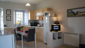 A modern kitchen with a dining area, featuring a refrigerator, microwave, and a TV on a cabinet. - Charming studio at the Manor with private garden and WiFi (Baubigny)