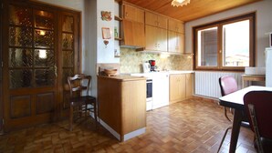 A kitchen with wooden cabinets, a central island, and a dining area with chairs. - Triolets 1 - 3 bedroom apartment in the centre (MORZINE)