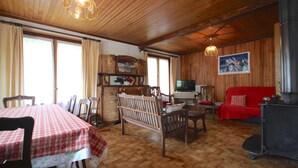 A cozy living room with a wooden floor, a dining table with a checkered tablecloth, a red sofa, a wooden bench, and a black stove. - Triolets 1 - 3 bedroom apartment in the centre (MORZINE)