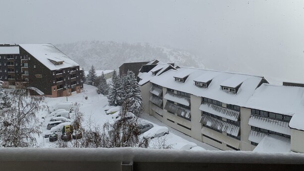 A snow-covered building with multiple balconies and a parking area with snow-covered cars.