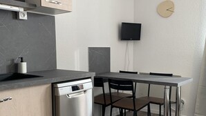 A compact kitchen with a dishwasher, a sink, and a flat-screen TV mounted on the wall.