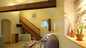 A cozy living room with a wooden staircase, a sofa, a small table, and potted plants.