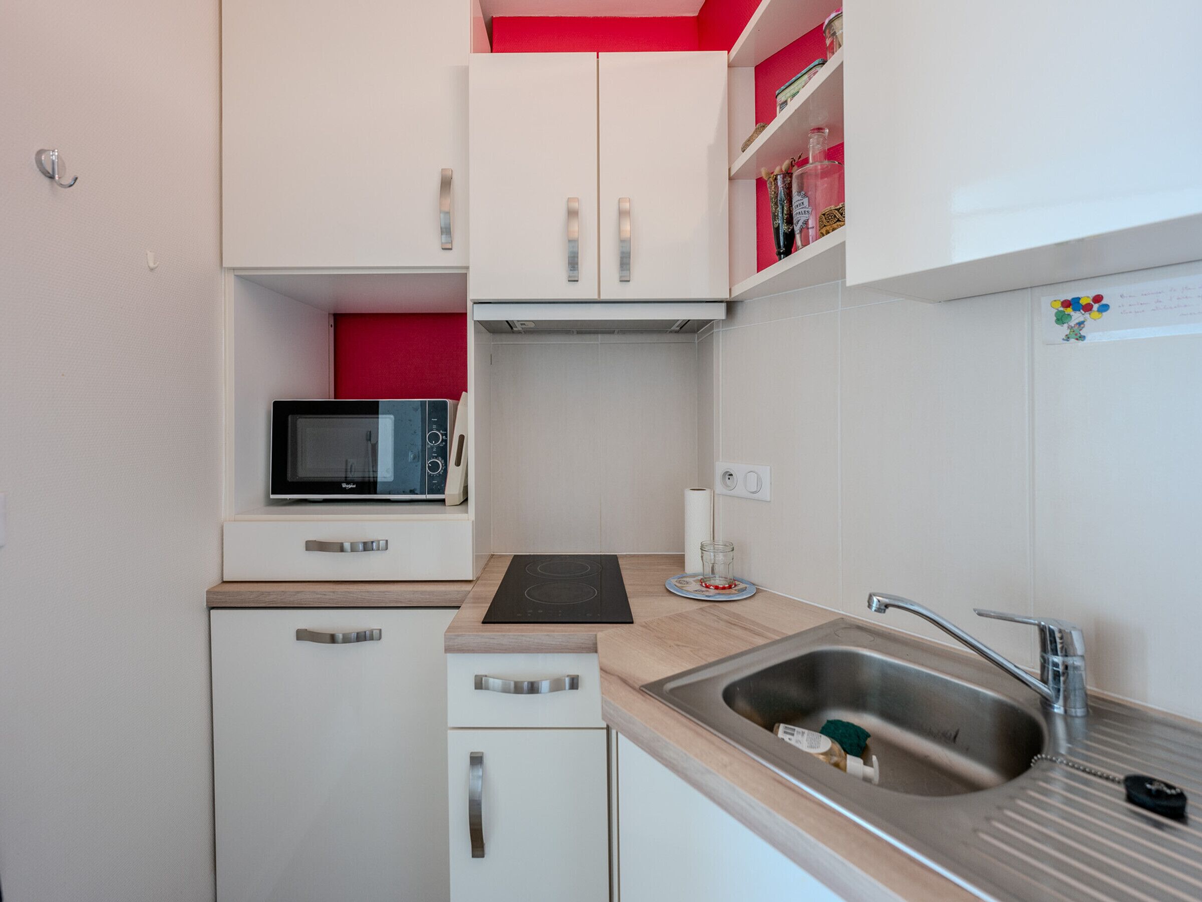A compact kitchen with white cabinets, a microwave, a sink, and a small countertop.