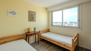 Ein Zimmer mit zwei Betten, einem kleinen Tisch mit Lampen, einem Spiegel und einem Fenster mit Blick auf die Stadt.
