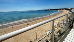 Ein Strand mit blauem Himmel, einem Pier in der Ferne und Gebäuden entlang der Küste.