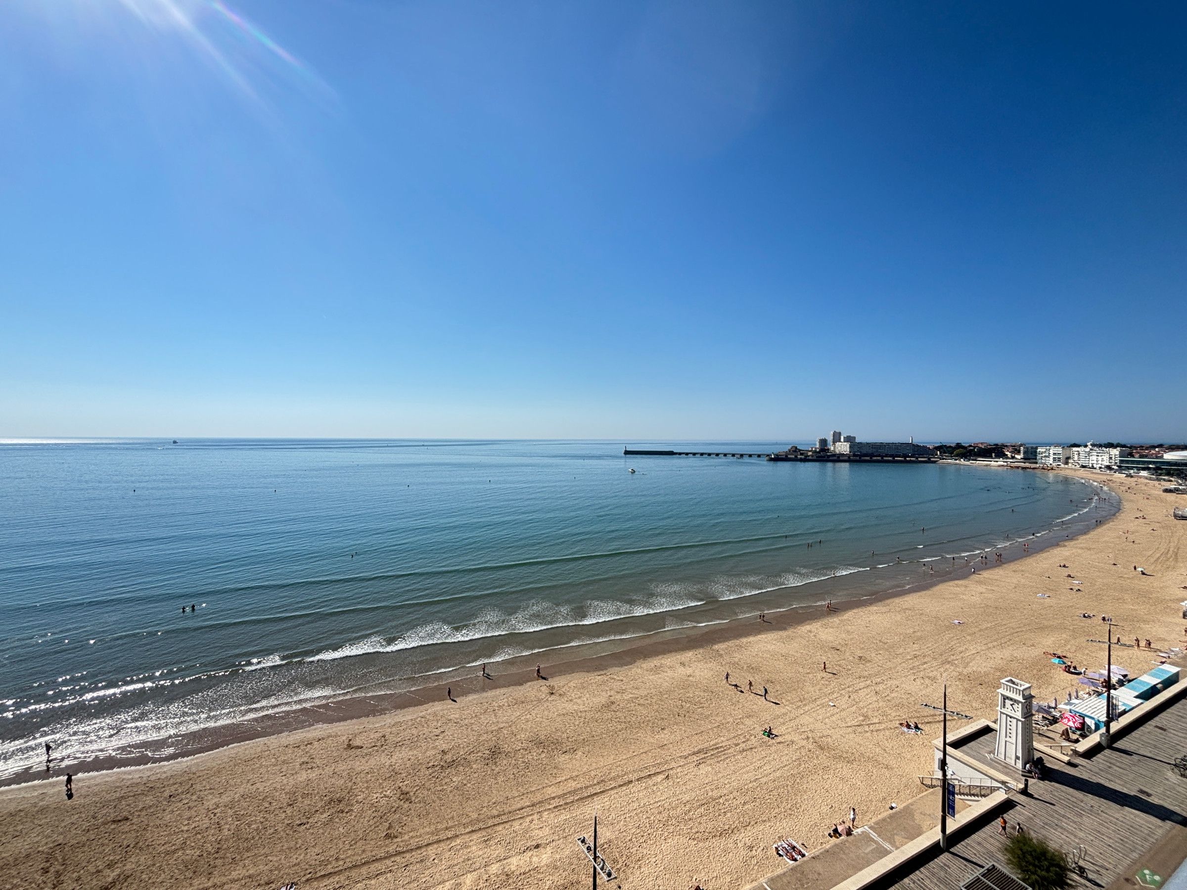 Uma praia com um píer que se estende para a água, uma torre do relógio e um calçadão com pessoas.