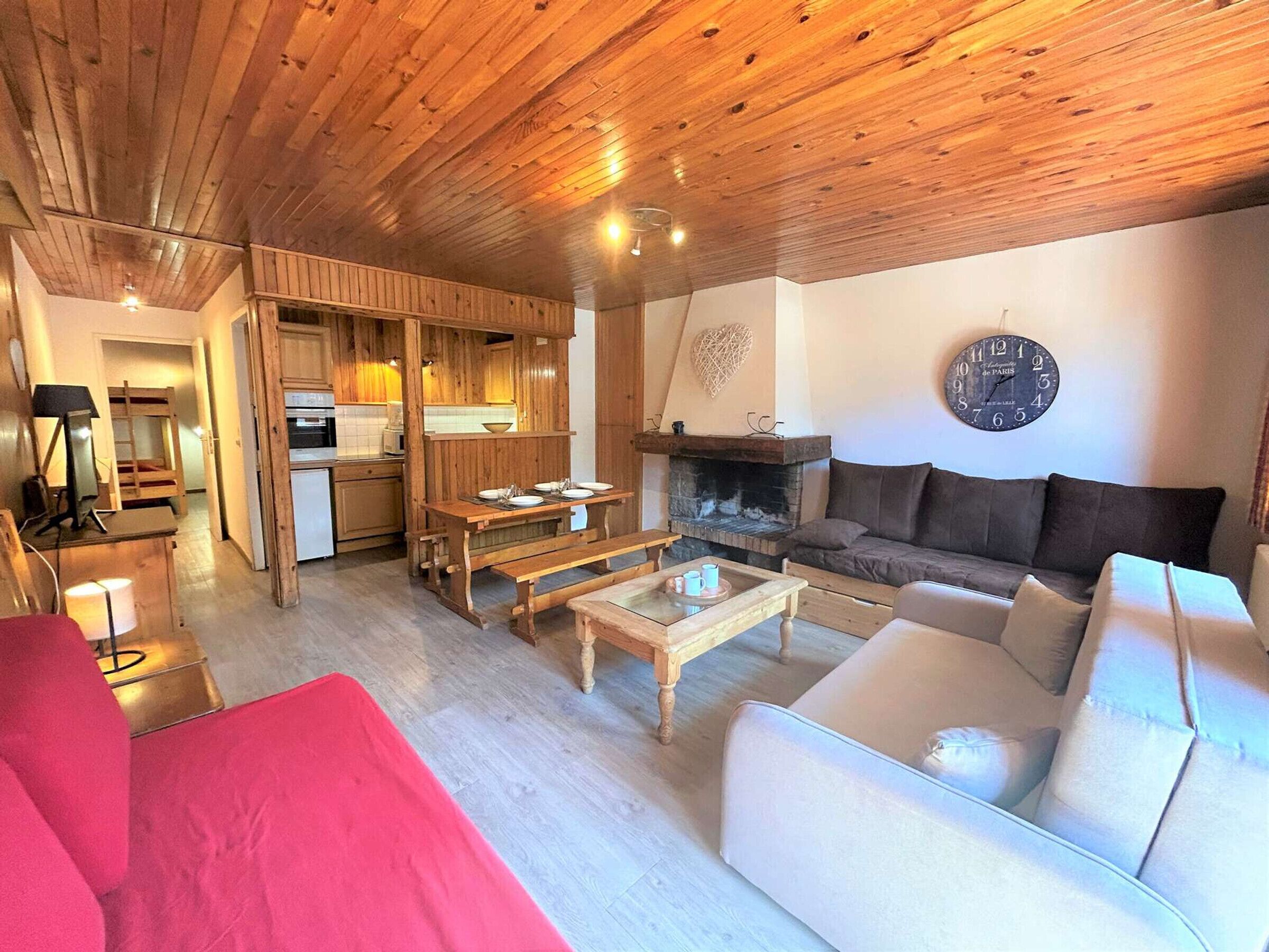 Een gezellige woonkamer met een open haard, een bank, een eettafel en een keuken op de achtergrond.
