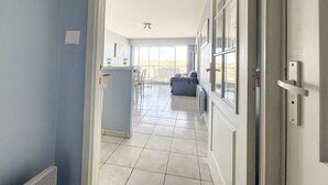 A spacious corridor with a kitchen area, a dining table, and a sofa in the background. - 1 Bedroom Apartment + Cabin with Sea & Dune View, 3rd Floor with Elevator (Cucq-Stella Plage)