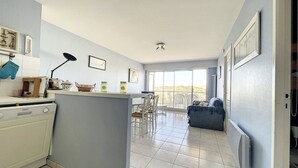 A spacious kitchen with a dining area, a large window, and a blue sofa. - 1 Bedroom Apartment + Cabin with Sea & Dune View, 3rd Floor with Elevator (Cucq-Stella Plage)