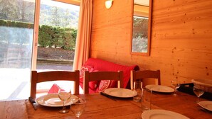 A wooden cabin dining room with a table set for two, a window with curtains, and a view of the outdoors.