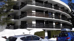 A multi-story building with balconies, surrounded by snow and trees.