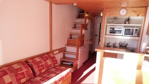 Un espacio habitable compacto con sofá, una zona de cocina con microondas y una escalera.