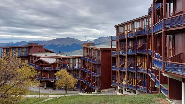 Un hotel de varios pisos con balcones y montañas al fondo.