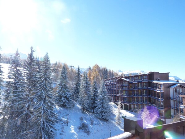 A snow-covered lodge with multiple floors and balconies, surrounded by snow-laden trees and mountains in the background.