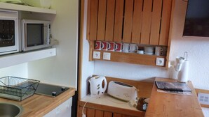 Una cocina compacta con microondas, tostadora y una repisa con tazas.