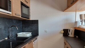 Ett kompakt kök med en svart bänkskiva, en diskho i rostfritt stål, en mikrovågsugn och en kaffebryggare.