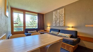 A room with a wooden dining table, two sofas, and a large window with a view of trees. - Ski-in/out studio for 5, Les Arcs 1800, pets allowed (Les Arcs 1800)