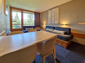 A room with a wooden dining table, two sofas, and a large window with a view of trees. - Ski-in/out studio for 5, Les Arcs 1800, pets allowed (Les Arcs 1800)