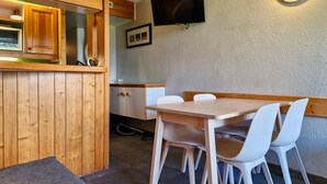 A wooden dining area with a table and chairs, a television mounted on the wall, and a kitchen area with cabinets and a microwave. - Ski-in/out studio for 5, Les Arcs 1800, pets allowed (Les Arcs 1800)