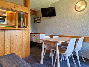 A wooden dining area with a table and chairs, a television mounted on the wall, and a kitchen area with cabinets and a microwave. - Ski-in/out studio for 5, Les Arcs 1800, pets allowed (Les Arcs 1800)