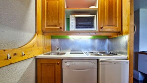 A compact kitchen with wooden cabinets, a built-in microwave, a sink, a dishwasher, and a stove. - Ski-in/out studio for 5, Les Arcs 1800, pets allowed (Les Arcs 1800)