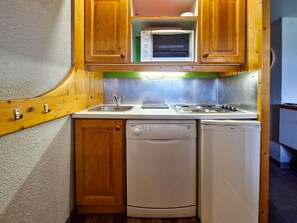 A compact kitchen with wooden cabinets, a built-in microwave, a sink, a dishwasher, and a stove. - Ski-in/out studio for 5, Les Arcs 1800, pets allowed (Les Arcs 1800)