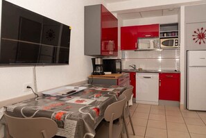 Une cuisine compacte avec des meubles de rangement rouges et blancs, un four à micro-ondes, une machine à café et une table à manger avec des chaises.