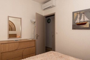 Une chambre avec une commode en bois, un miroir, une lampe de chevet, un lit moelleux, une porte donnant sur une salle de bain et un tableau représentant un voilier.