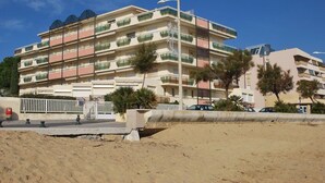 Un hotel a più piani con balconi, una spiaggia sabbiosa in primo piano e un cielo azzurro limpido.