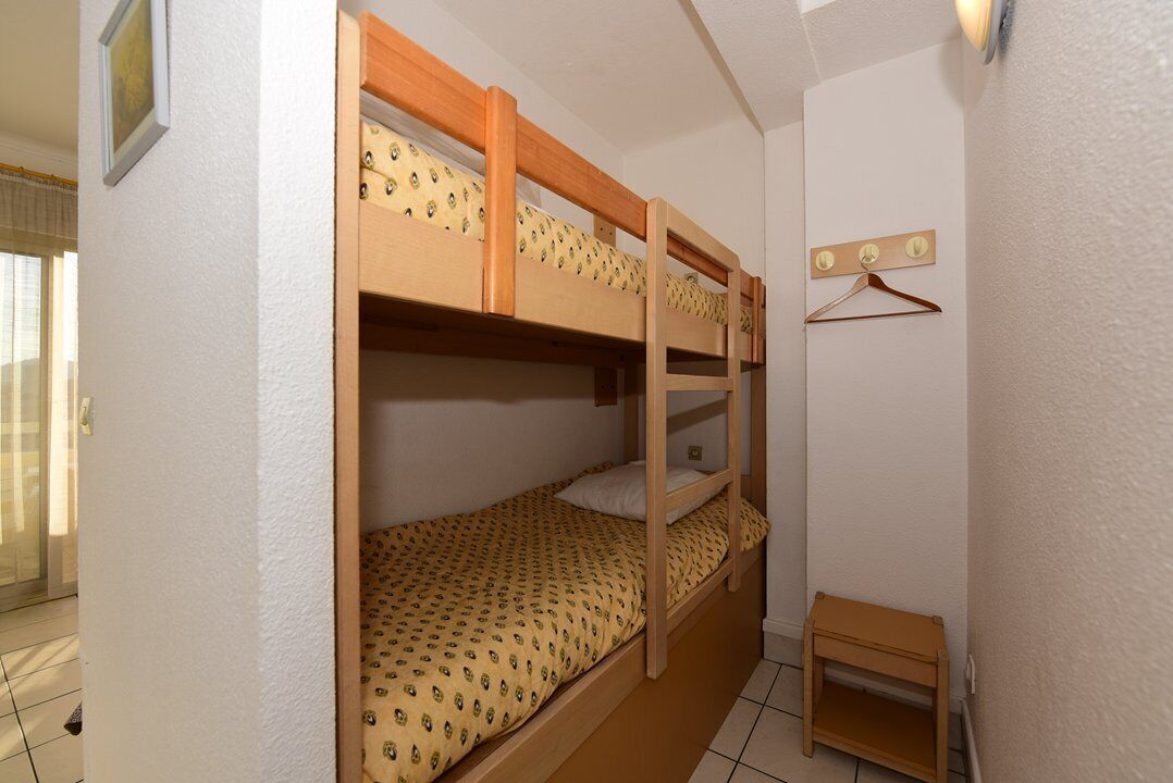 Uma cama beliche com colcha estampada, uma pequena mesa de cabeceira de madeira e um luminário fixado na parede.