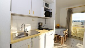 Angolo cottura compatto con lavello, forno a microonde e macchina del caffè. C'è una zona pranzo con tavolo e sedie.