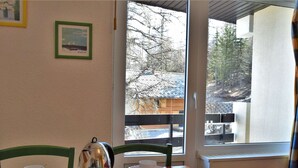 A dining area with a table set for two, a kettle, a box of cereal, and a window with a view of trees and a building. - Mountain Studio, 4 Sleeps, Ski-In/Ski-Out, Free Parking, Risoul 1850 (Risoul)