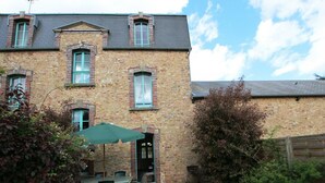 A stone building with a gravel courtyard, a table with chairs, and a green umbrella. - Comfortable cottage with WiFi and pets allowed (Périers)