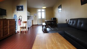 A spacious living area with a wooden table, a black leather sofa, and a kitchen in the background. - Comfortable cottage with WiFi and pets allowed (Périers)