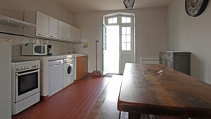 A kitchen with white cabinets, a microwave, an oven, and a washing machine. There's a wooden table and a broom leaning against the wall. - Comfortable cottage with WiFi and pets allowed (Périers)